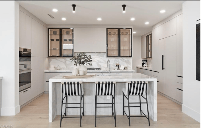 Contemporary white kitchen with a marble waterfall island and three striped bar stools.