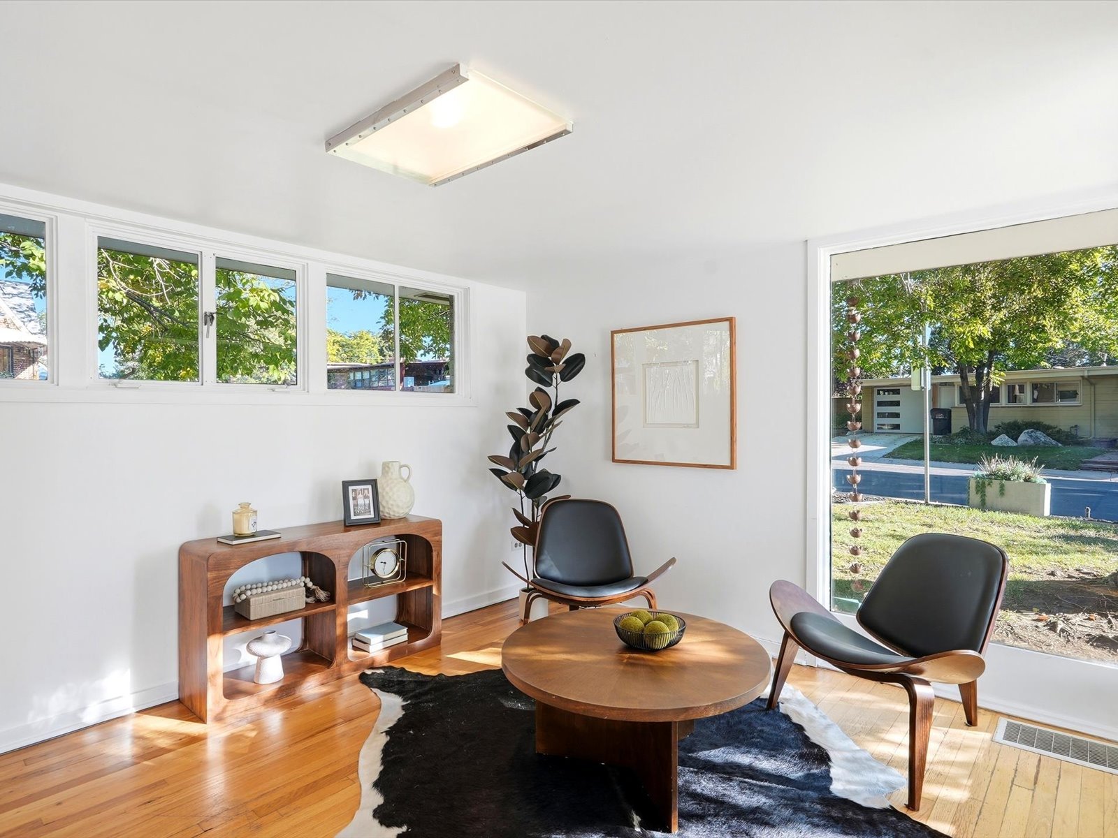 Mid-century modern living area with lounge chairs, hardwood floors, and a large glass door to the yard.