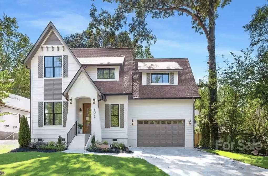 White two-story house with dark shingle roofs, a gray garage, and a landscaped front lawn.