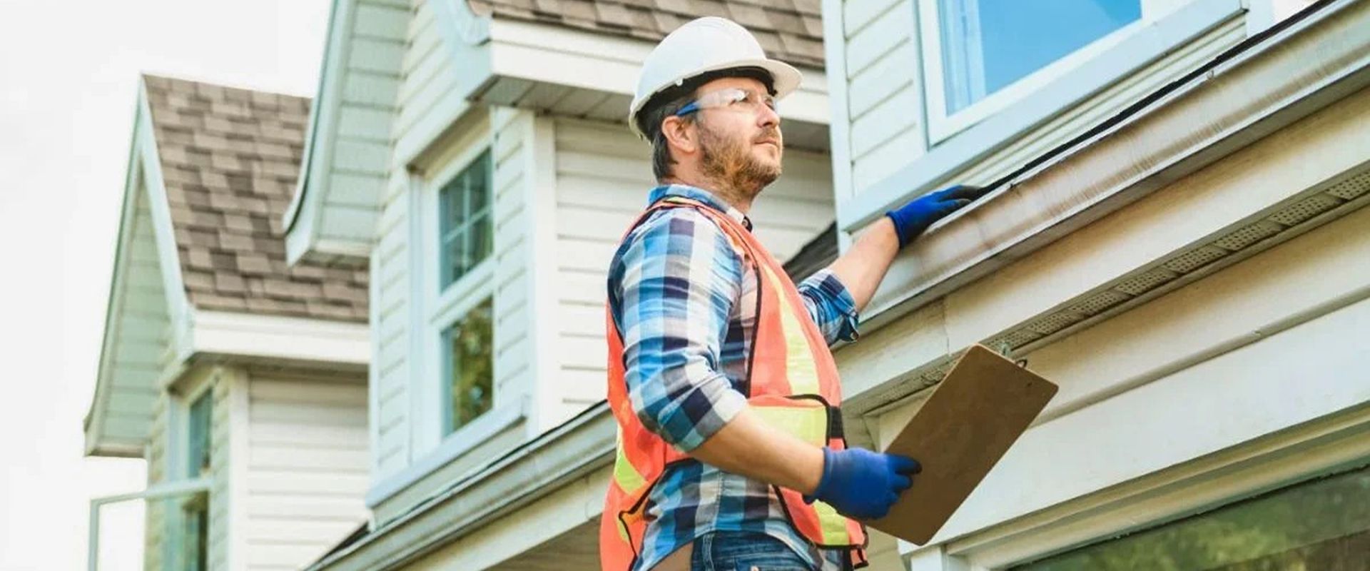 Home inspector examines a house’s white siding while holding a clipboard.