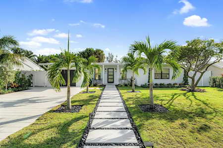 Modern single-story home with a palm-lined stone walkway and broad driveway.