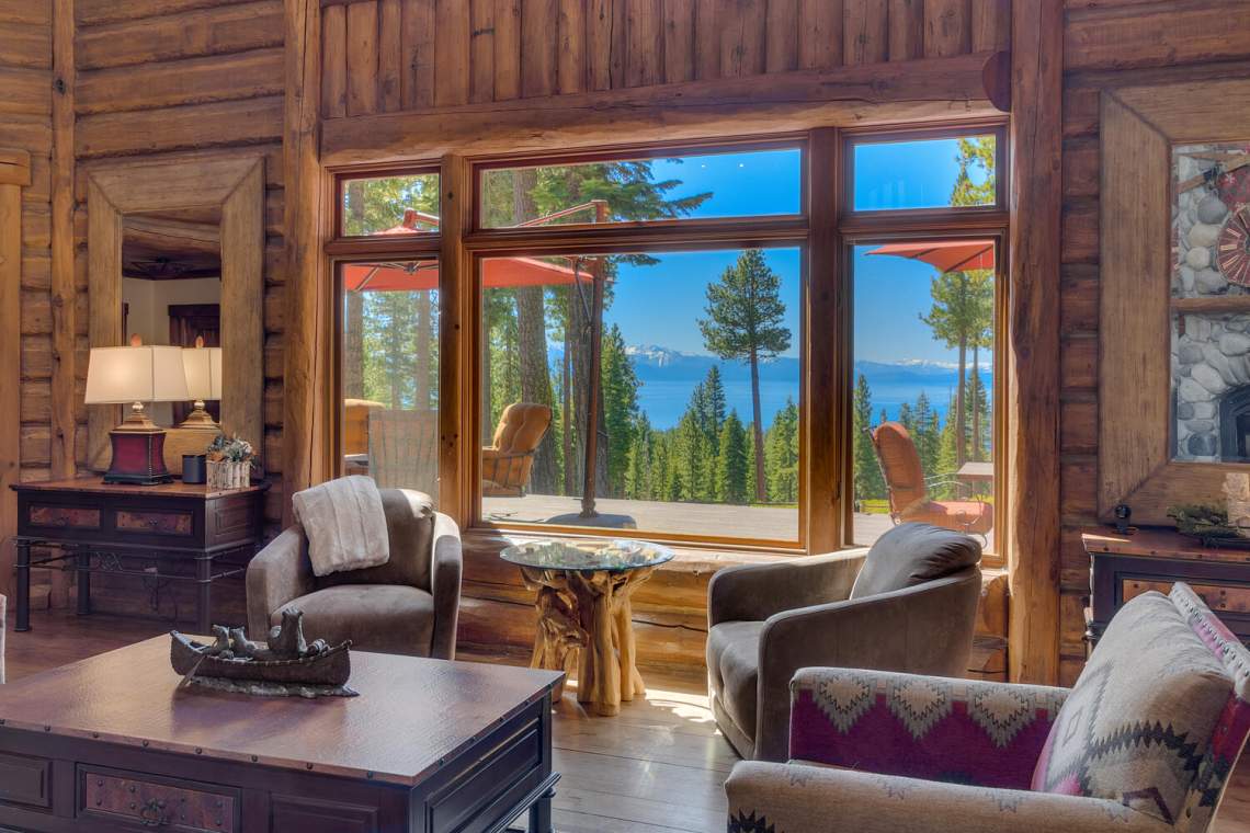 Rustic living room with a large window overlooking Lake Tahoe and distant mountains.