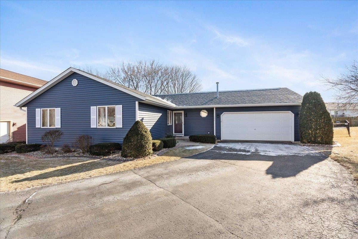 Exterior view of a well-kept blue ranch-style single-family home with an attached two-car garage and paved driveway, representing the highly competitive starter homes under $450,000 in Sun Prairie, WI that often sell in a single weekend.