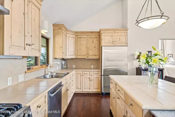 Kitchen with pale wood cabinets, stainless-steel appliances, tiled counters, and a central island.