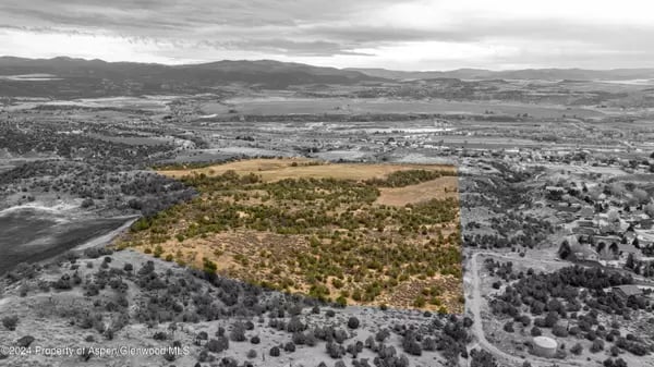 Aerial view of a highlighted scrub-covered parcel with rural homes and distant mountains.