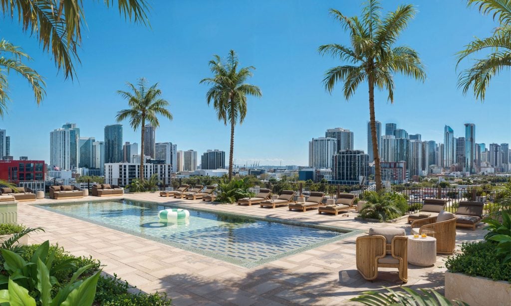 Rooftop pool and furnished sun deck framed by palm trees, with the Miami skyline beyond.