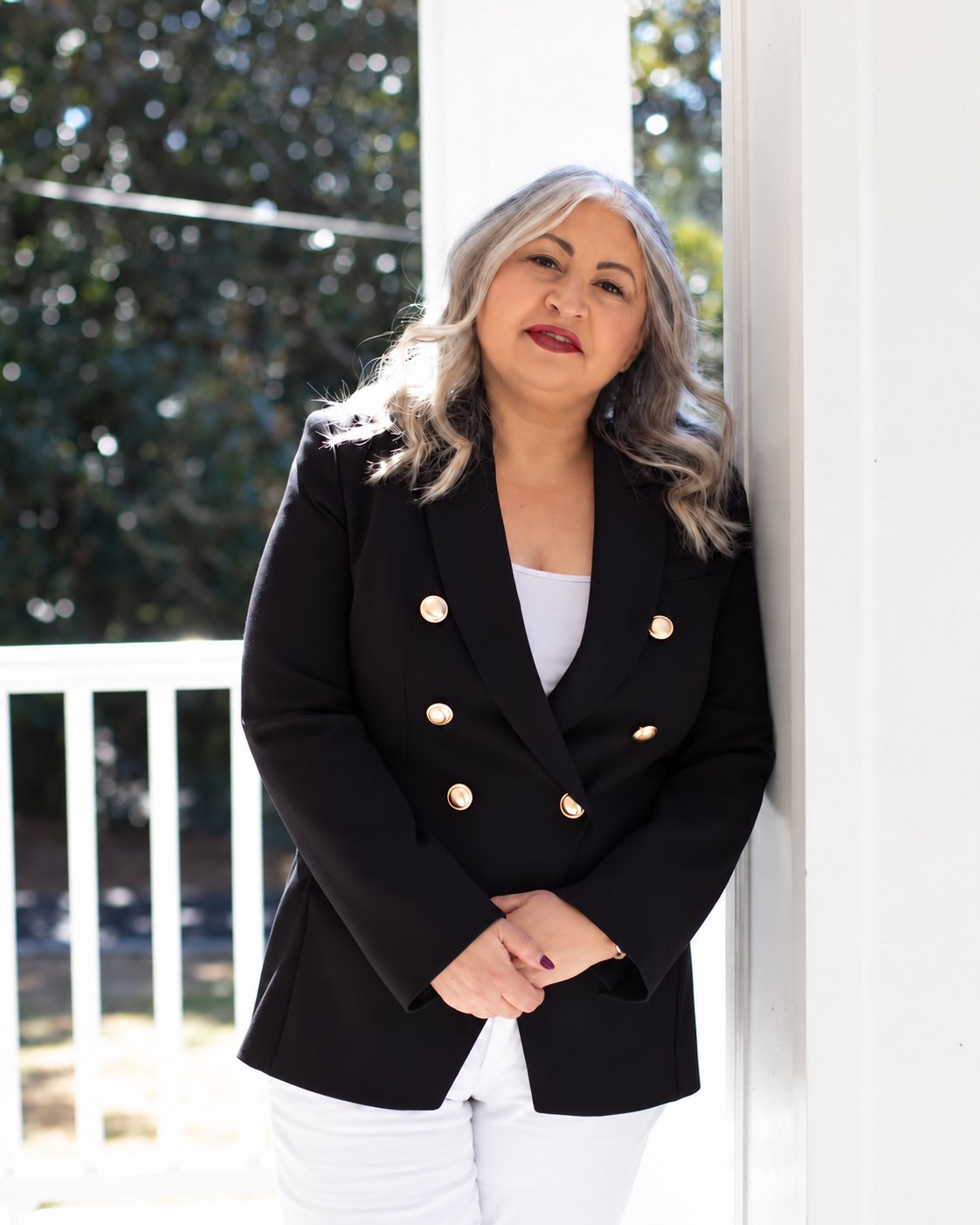 Brenda Plaugher standing beside a white porch railing in a black blazer with gold buttons.