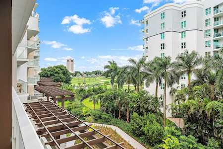 Condominium buildings overlook landscaped grounds with palm trees and a wooden pergola.