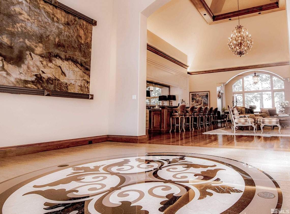 Foyer with an ornate marble floor medallion, chandelier, and arched windows overlooking the living area.