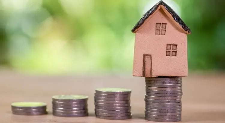 A small house model perched on stacks of coins, symbolizing real estate investment, savings, or property value.