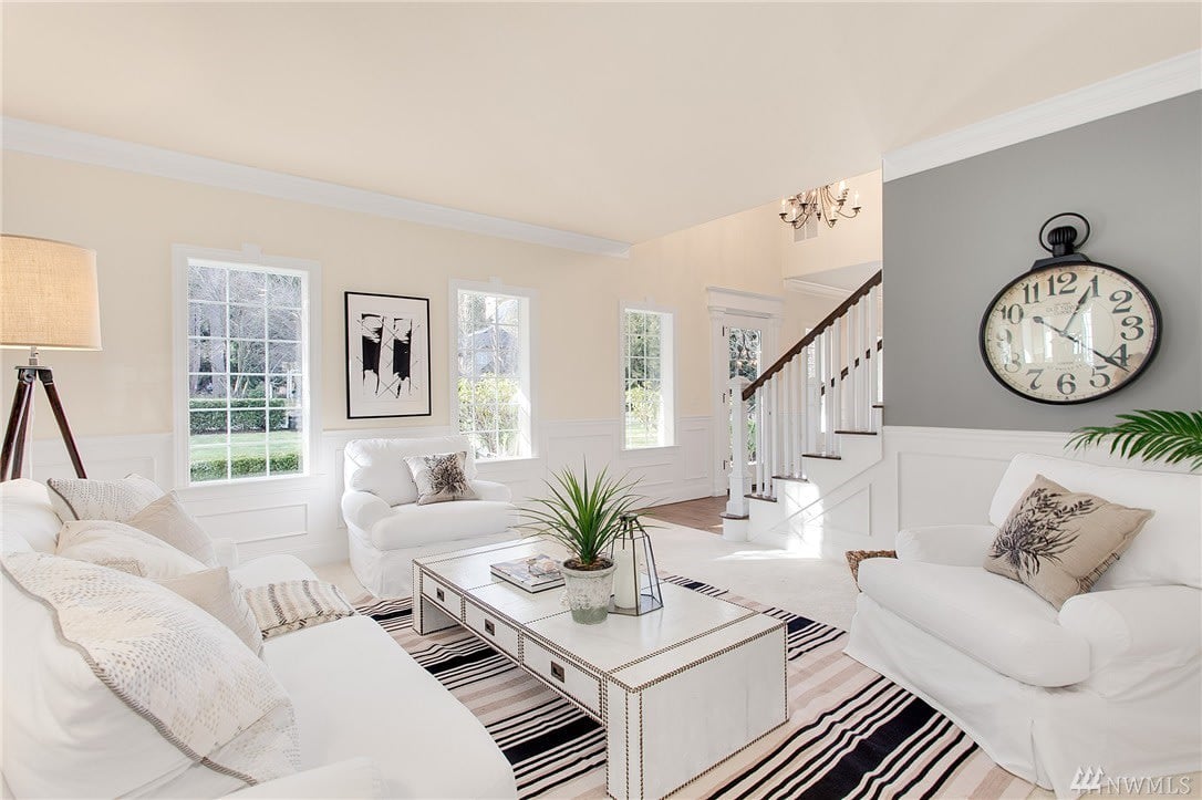 Living room with white sofas, a striped rug, tall windows, and a staircase.