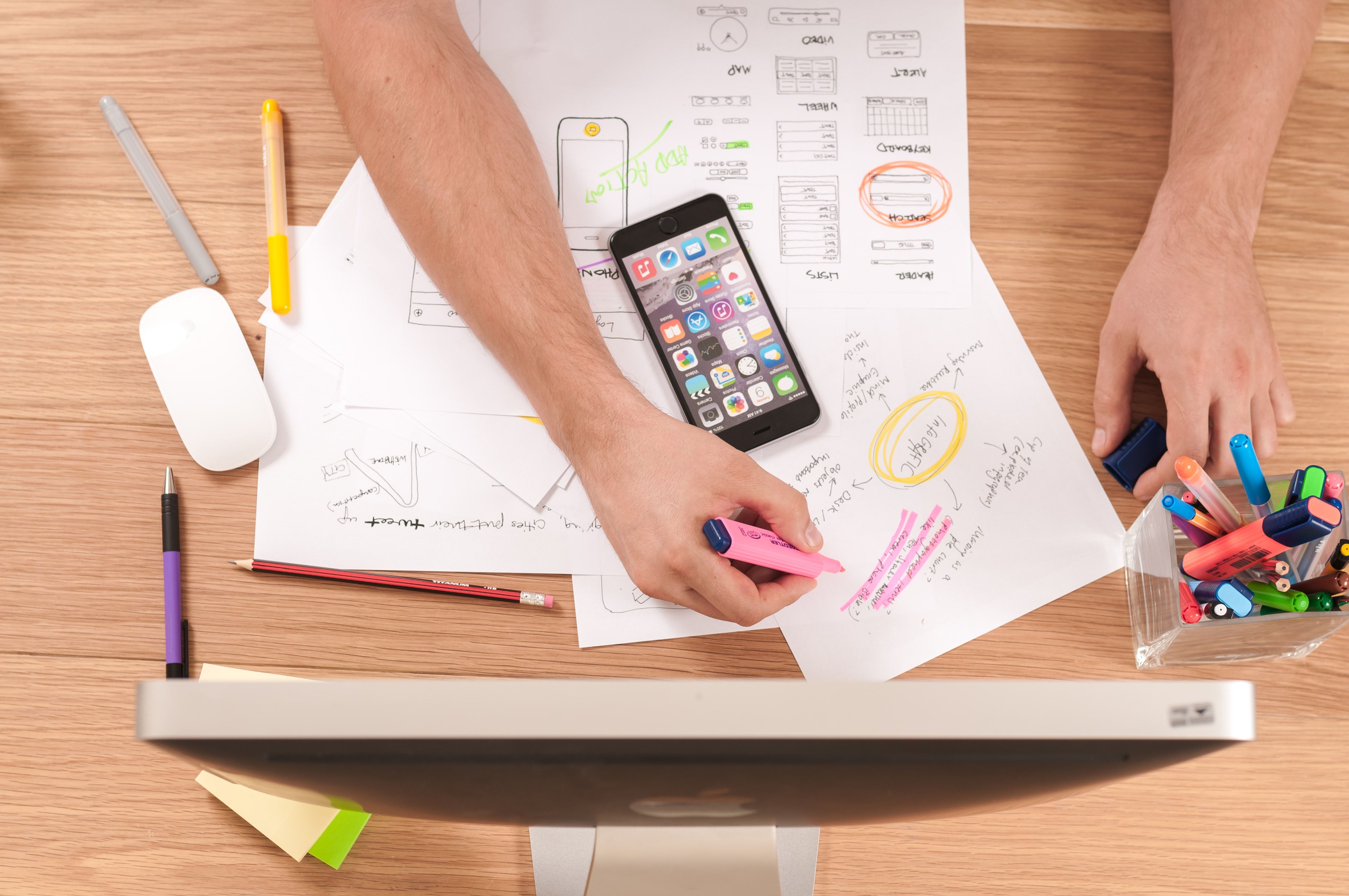 Person highlights handwritten notes and sketches beside a smartphone on a wooden desk.