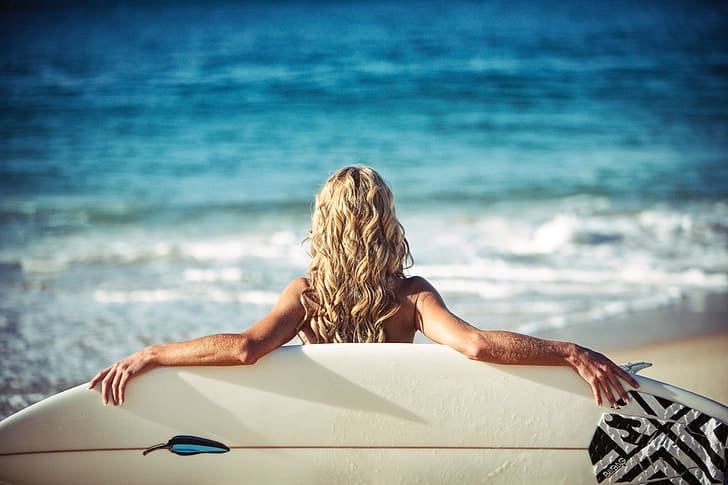 a person sitting on the beach with his surfboard