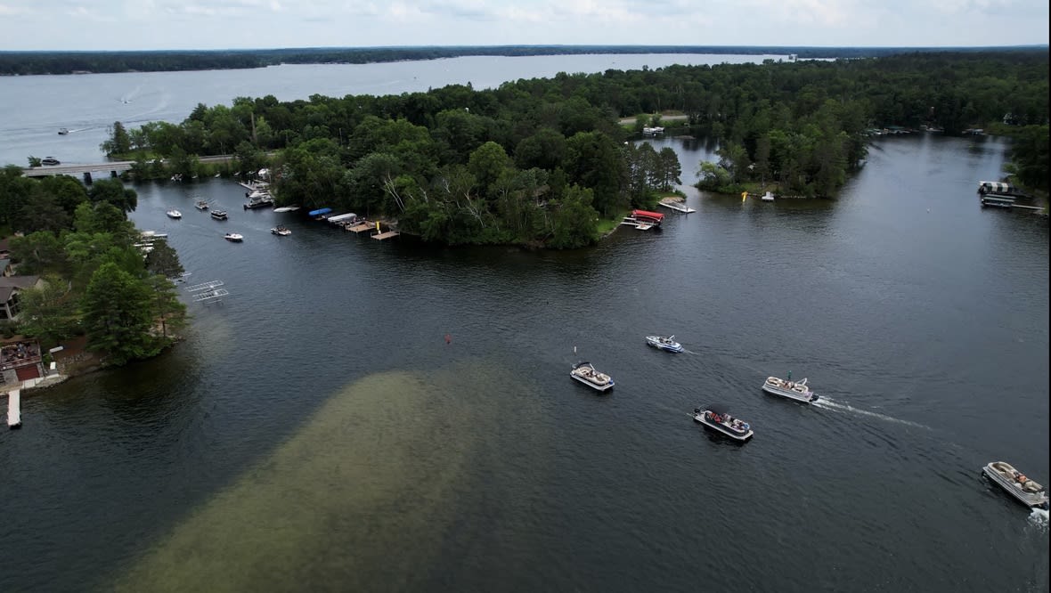 Crosslake neighborhood frames a serene blue lake, sailboats dotting the glistening water under a clear sky.