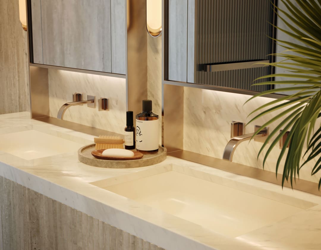 Marble double-sink bathroom vanity with brass faucets, large mirrors, and toiletries.