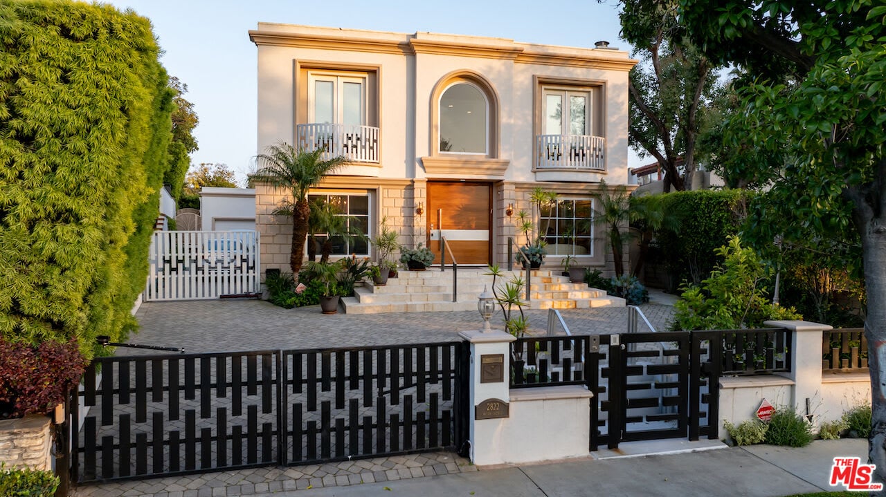 A grand, multi-story house with a light-colored stucco exterior, prominent arched windows, and a brown front door