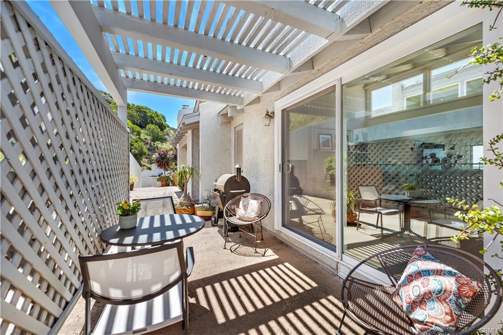 Furnished patio beneath a white pergola with lattice screens, outdoor seating, and a barbecue.