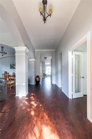 Bright hallway with dark wood floors, a chandelier, and arched openings to adjoining rooms.