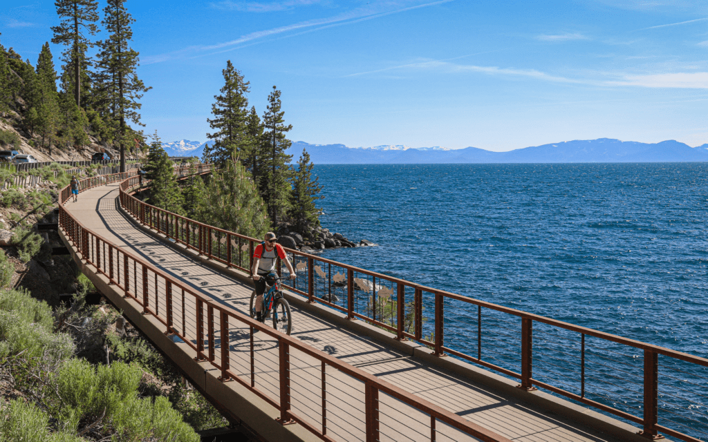 Scenic view of a cyclist riding along the East Shore Bike Path near Incline Village, with Lake Tahoe and surrounding mountains in the background.