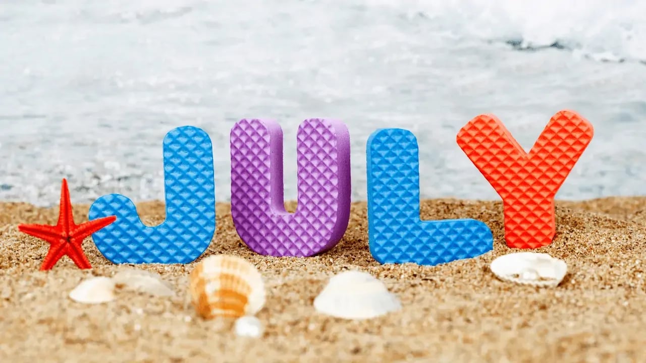 Colorful letters spelling out "JULY" on a sandy beach with seashells and a starfish, representing a summer theme.