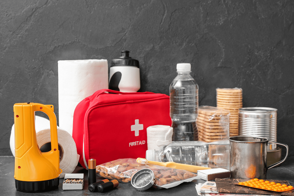 Emergency supplies with a red first-aid kit, flashlight, bottled water, canned food, and crackers.
