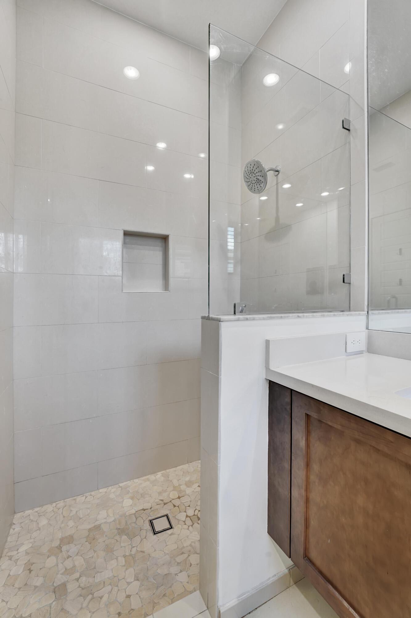 Modern bathroom with a glass shower, pebble floor, and wood vanity.