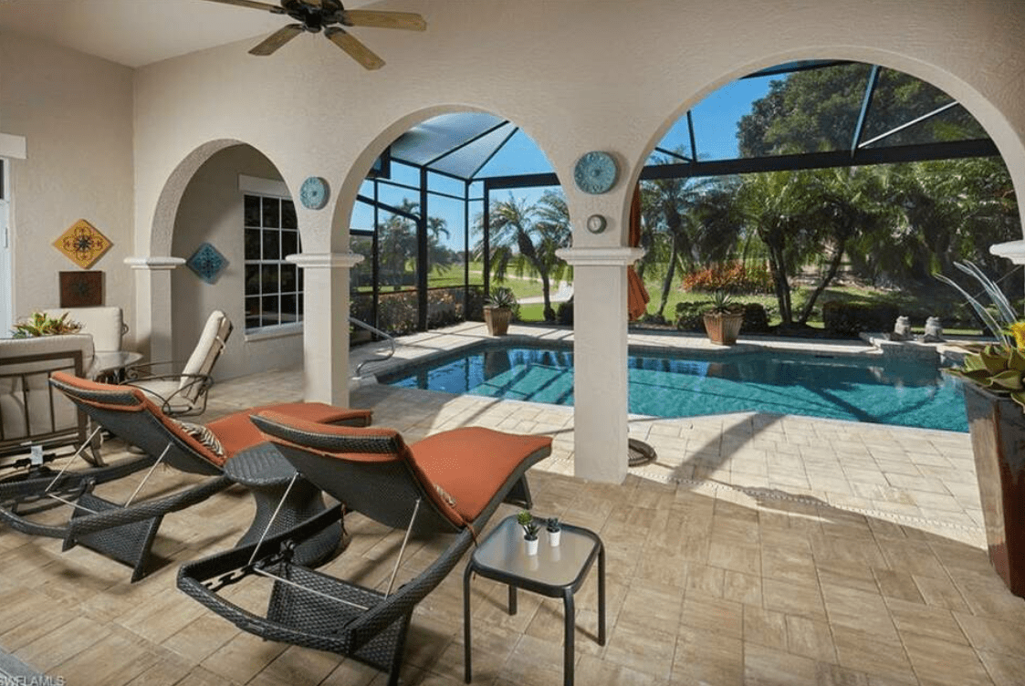  A spacious outdoor patio with a screened-in pool area, viewed from under a covered lanai.