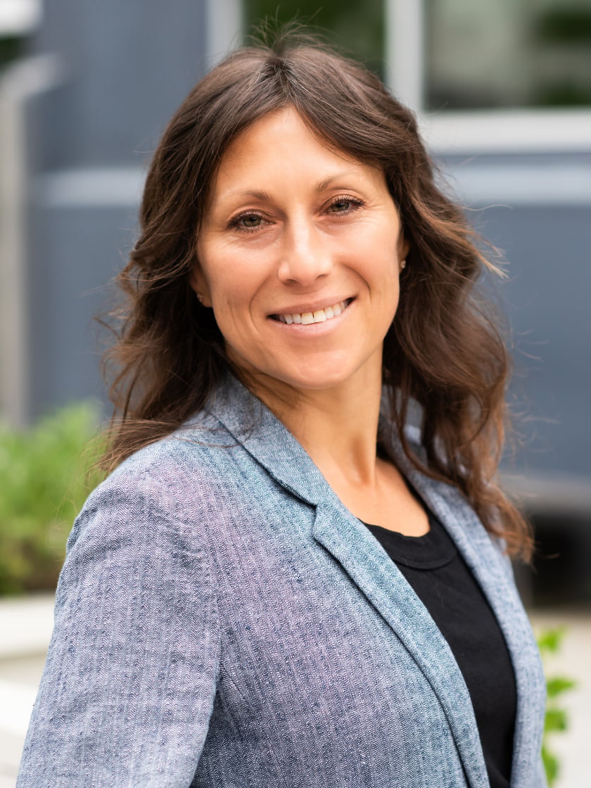 Havah Hahn-Schuman, smiling in a blue-gray blazer outdoors.
