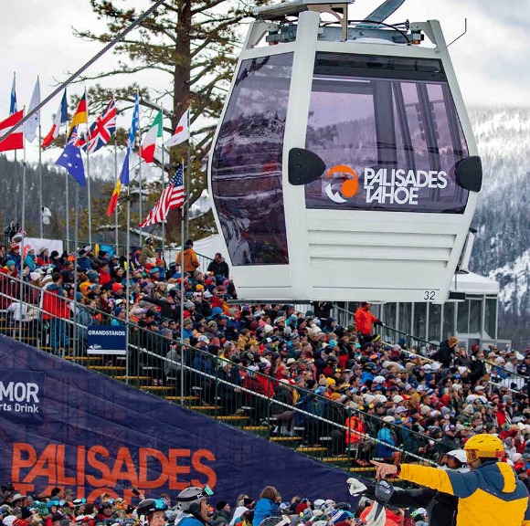Palisades Tahoe gondola above crowded winter event grandstands and rows of international flags.
