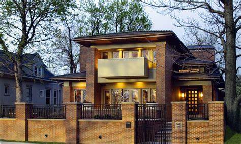 Two-story brick house, with black metal fence, hipped roof, asphalt shingles, second-floor balcony, framed windows, concrete path, and trees in front yard.