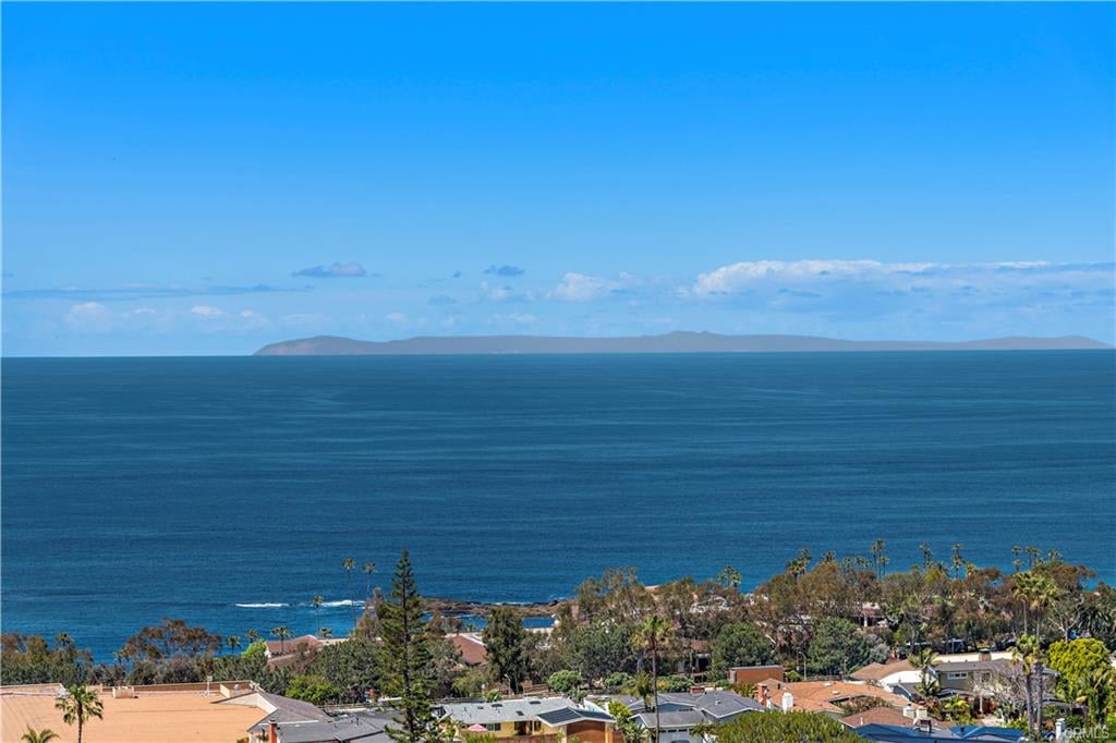 Ocean view over coastal homes, with a distant island beneath a clear blue sky.