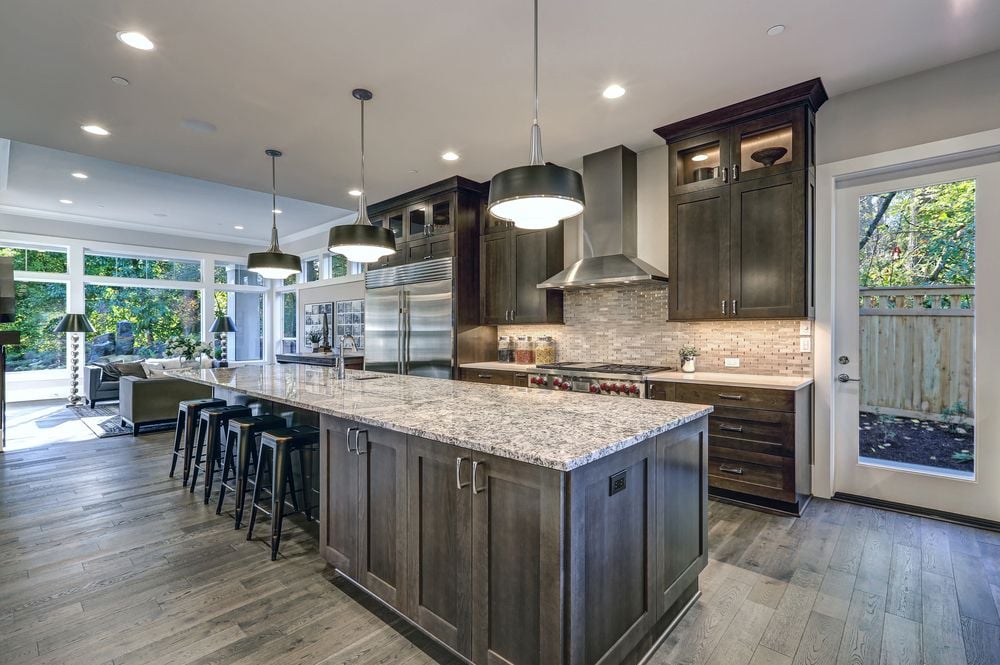 Modern kitchen with dark wood cabinets, a large granite island, and an open living area.