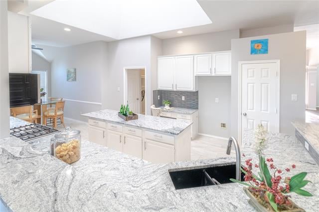 Open-plan kitchen with white cabinets, gray stone counters, a large island, and a dining area beyond.
