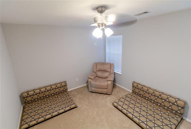 Carpeted bedroom with two patterned daybeds, a tan recliner, and a ceiling fan.