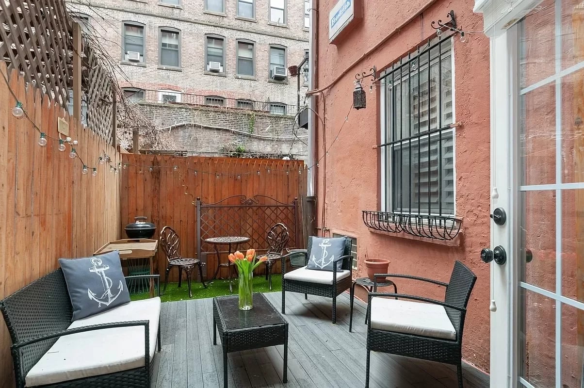 Private patio with wicker seating, artificial turf, wooden fencing, and string lights.