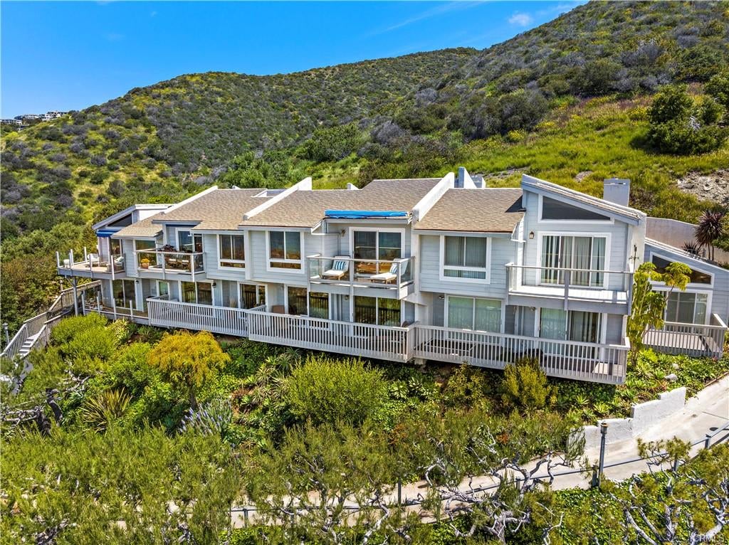 Coastal residential building with several balconies nestled against a green hillside.