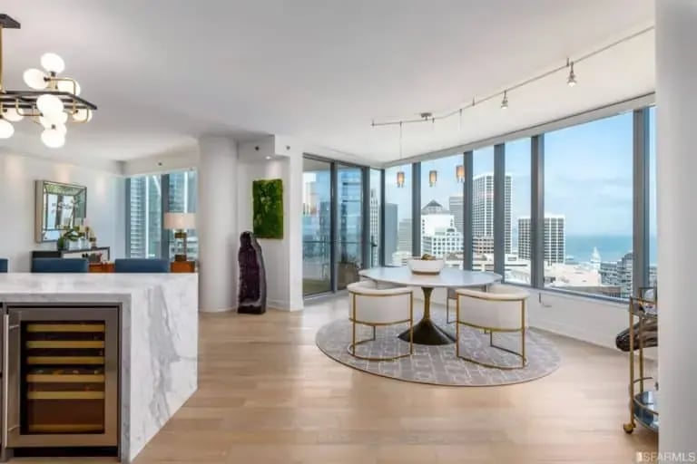 Interior view of Residence 34B at Lumina, 201 Folsom Street, San Francisco, showcasing a dining area with floor-to-ceiling windows overlooking city buildings, and partial views of the modern kitchen and living room.