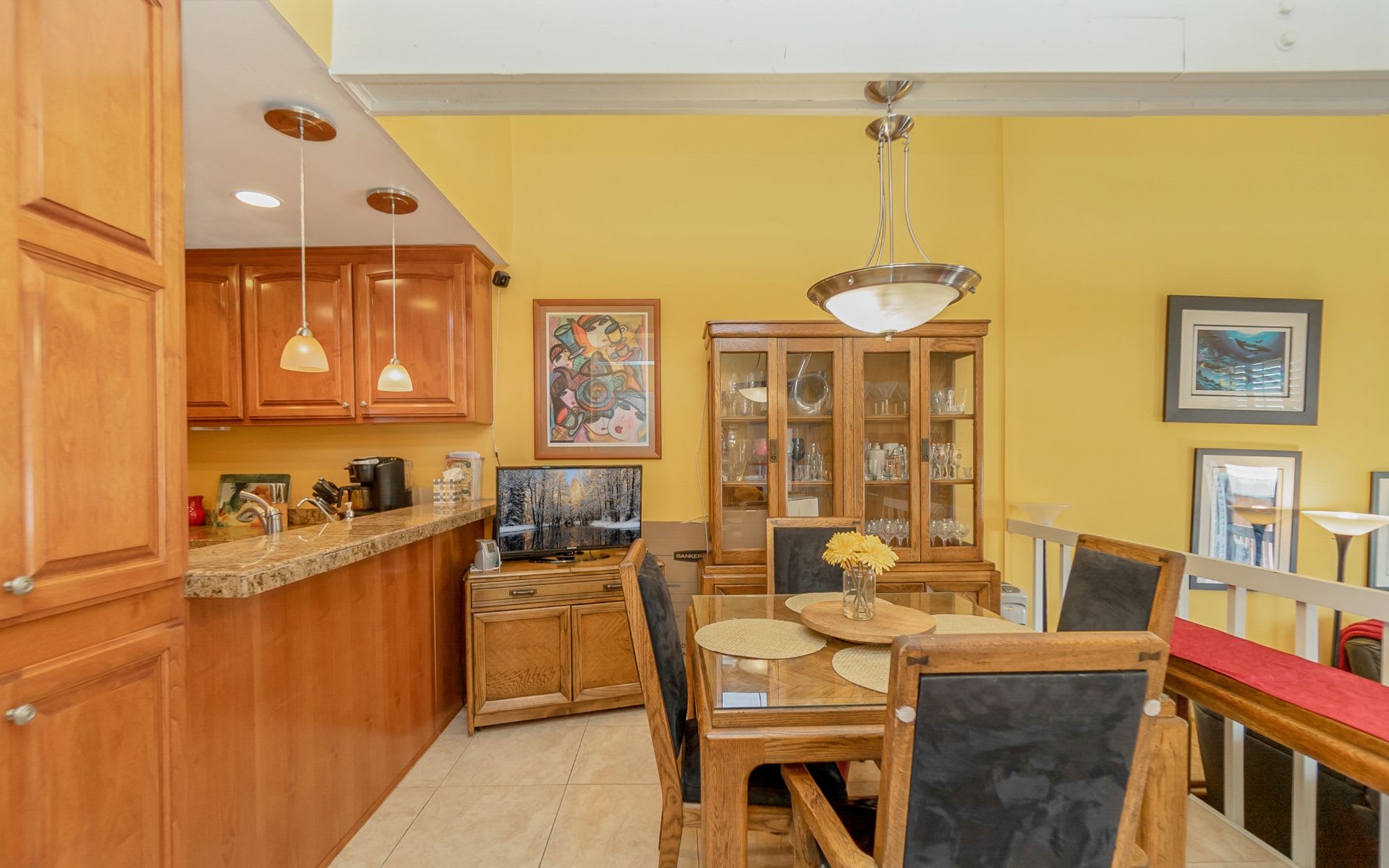 Dining room beside an open kitchen, with wood cabinetry and a glass-top table.