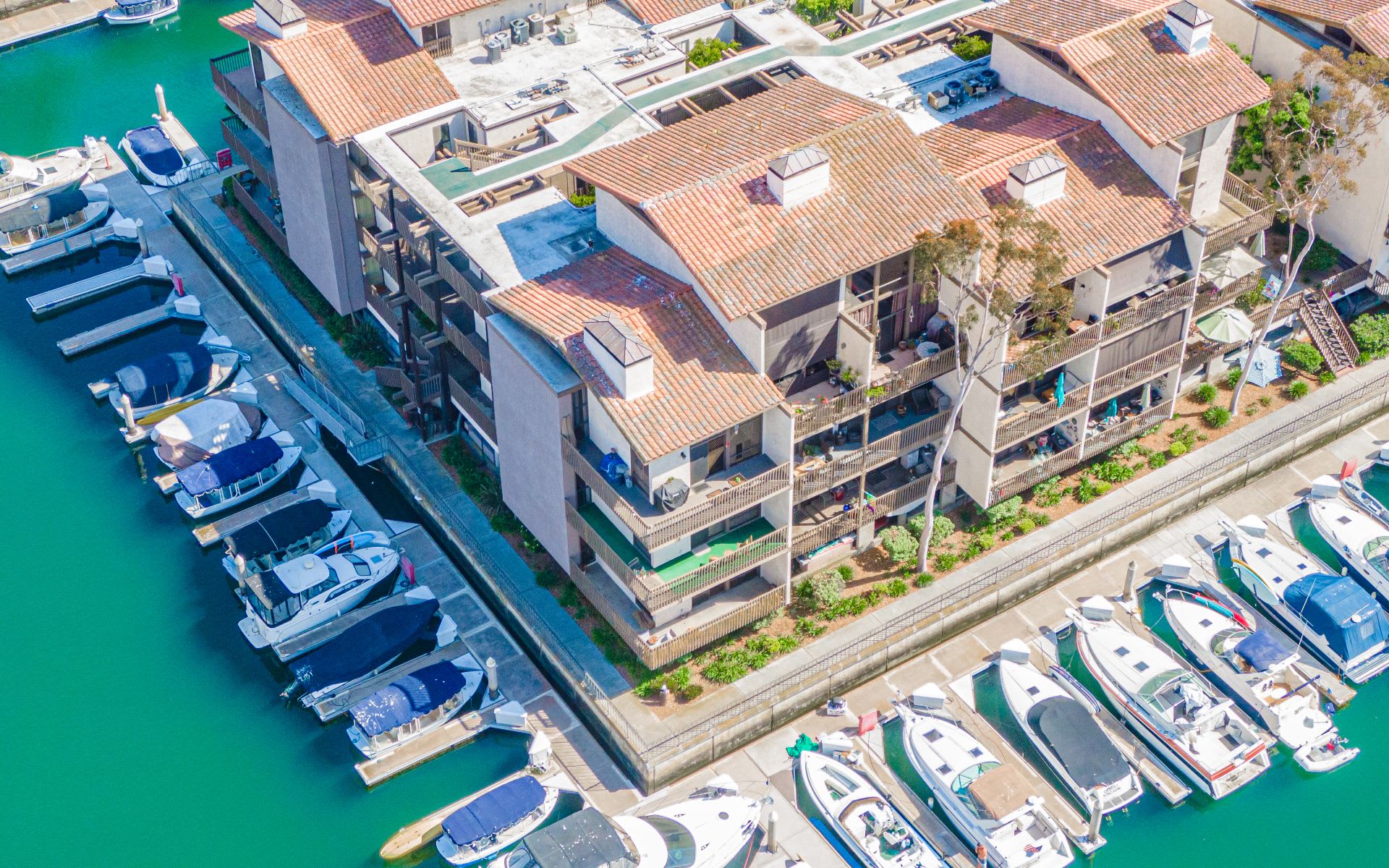 Waterfront condominium complex beside marina docks filled with boats, viewed from above.