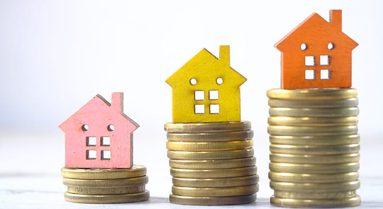 An image with stacks of coins supporting small house models of different colors, along with a house-shaped key.