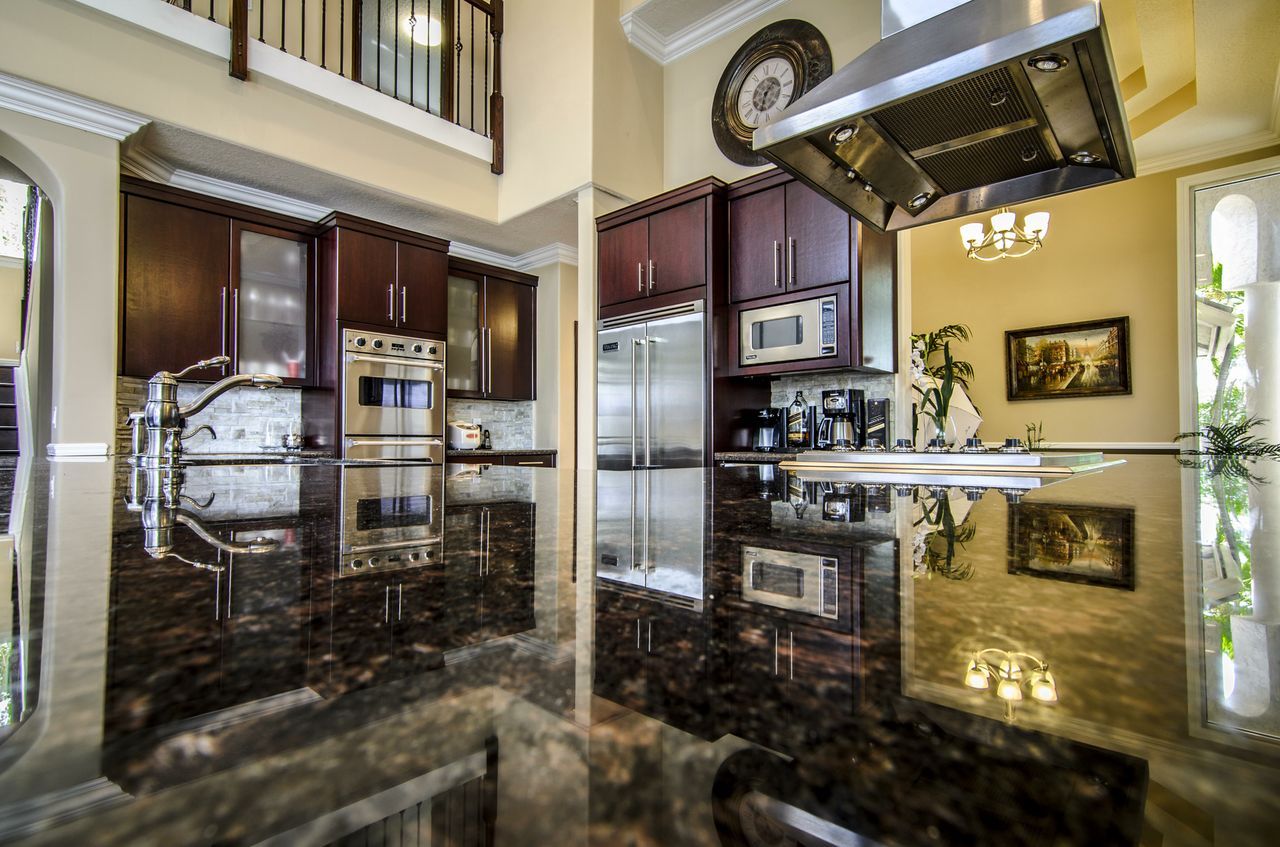 Kitchen with dark cherry cabinets, stainless steel appliances, and a large reflective granite island.