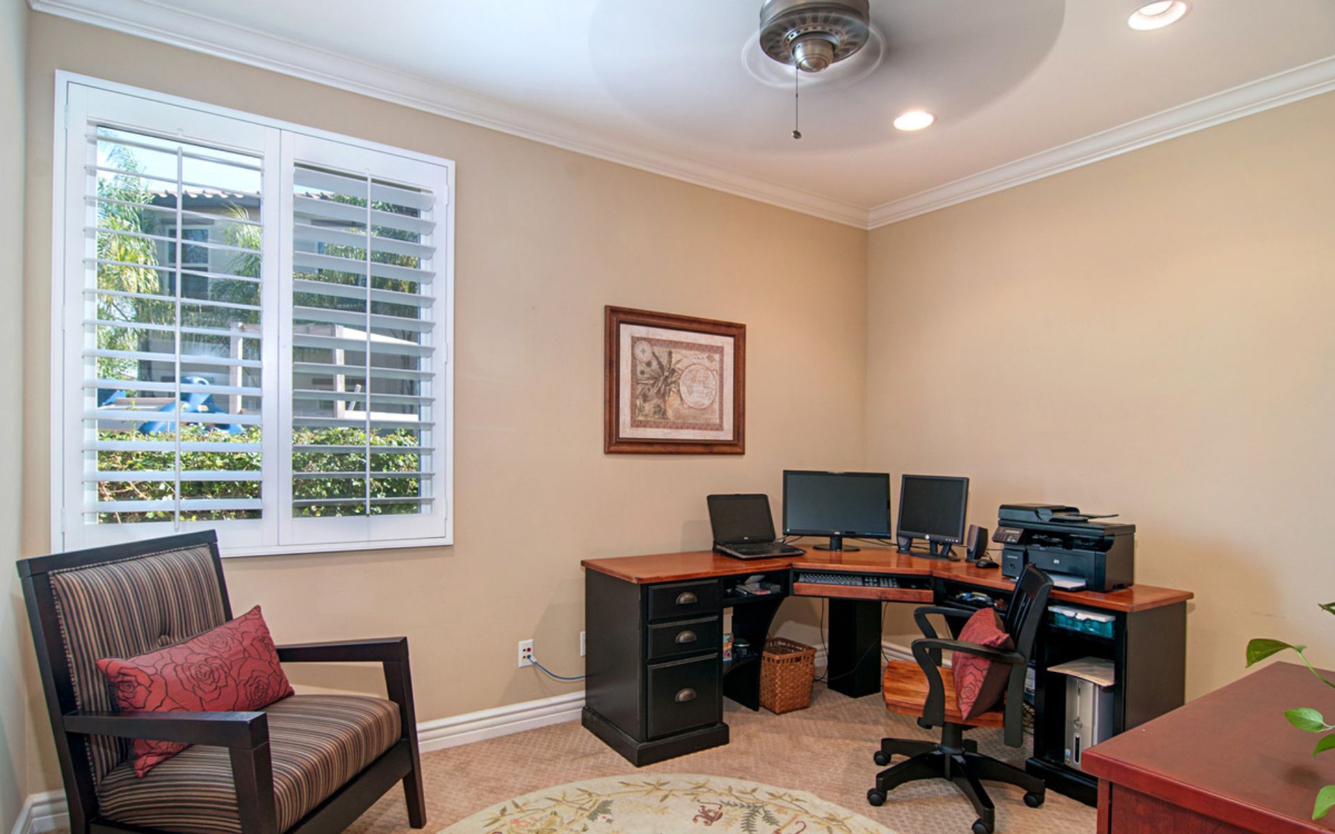 Home office with a curved wooden desk, computer monitors, and a shuttered window.