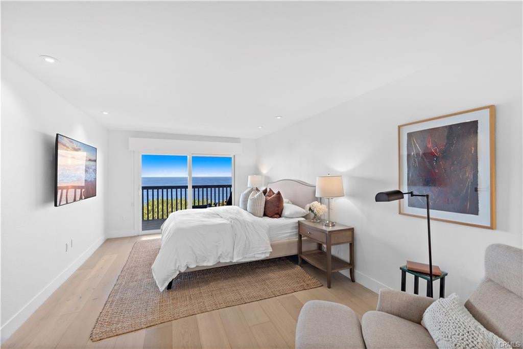 Bedroom with a white bed and sliding doors opening to a balcony overlooking the ocean.