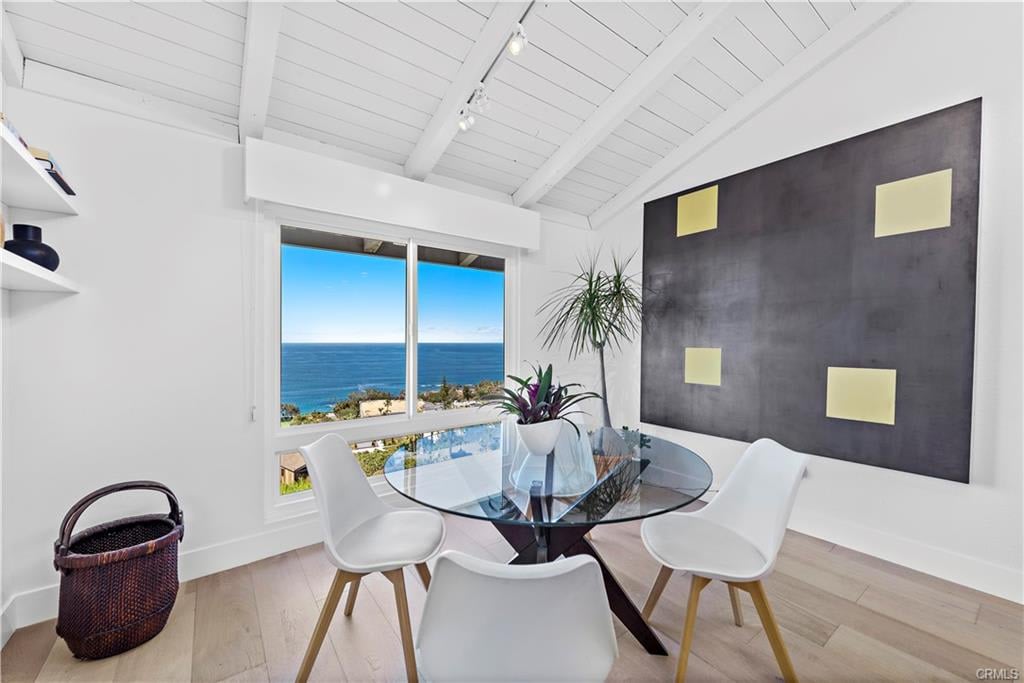 Dining area with a glass table and white chairs, ocean views through a large window.