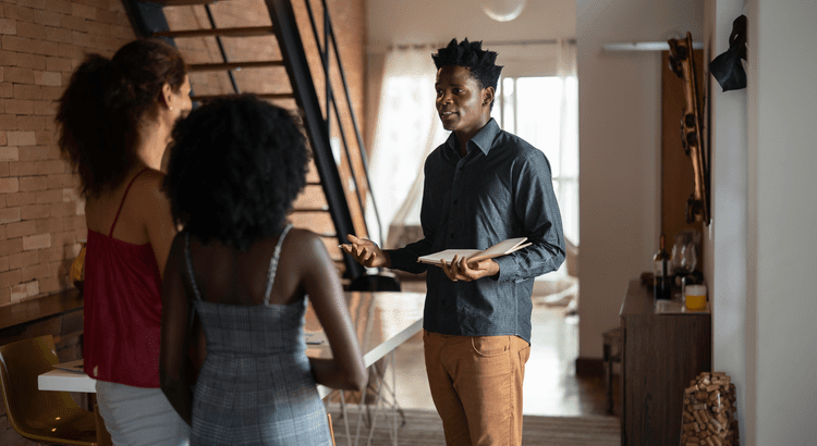 man and two women standing in a two story home having a discussion over a notebook