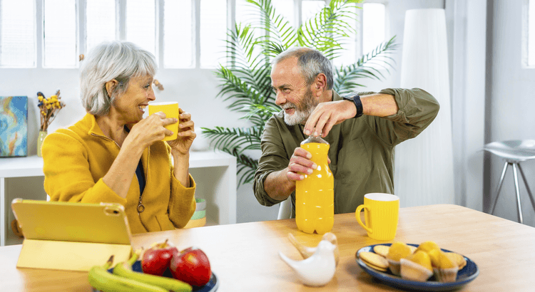 Older couple sharing breakfast at a bright kitchen table with yellow mugs and fresh fruit.