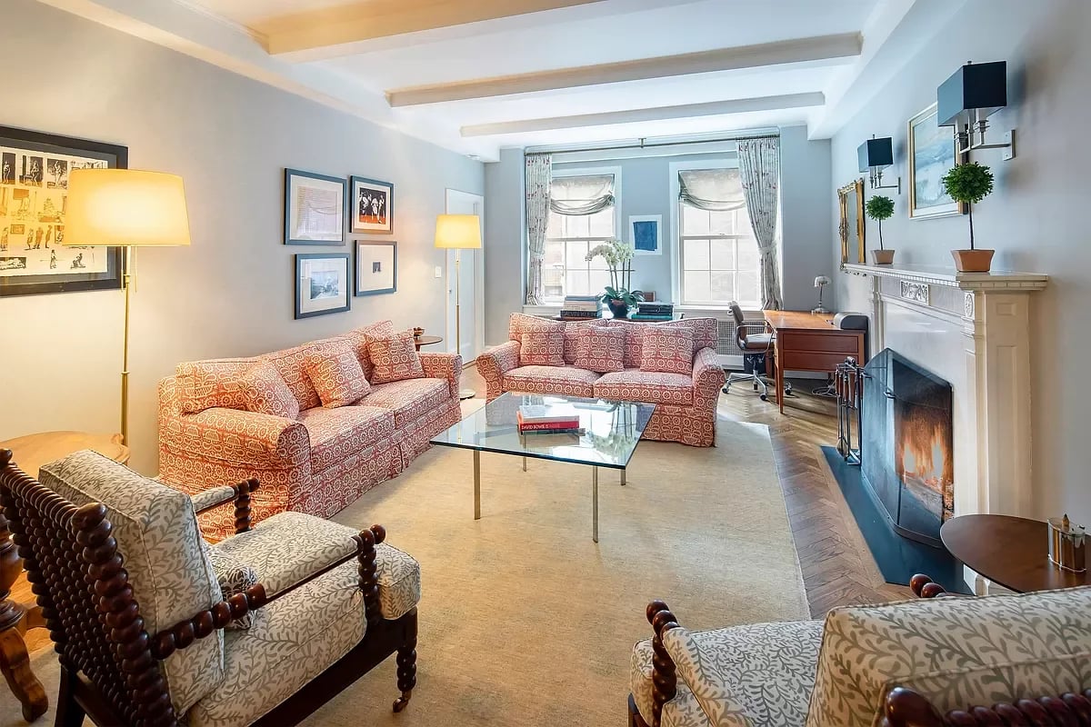 Living room with patterned seating, a glass coffee table, tall windows, and a fireplace.