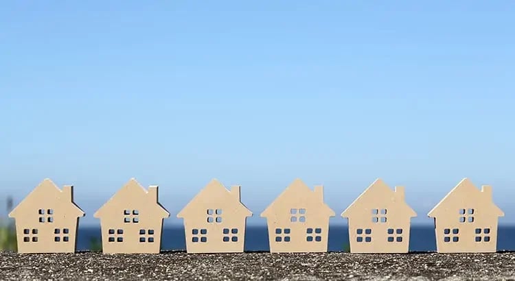 A row of small model houses set against a blue sky background, representing a housing development or real estate concept.