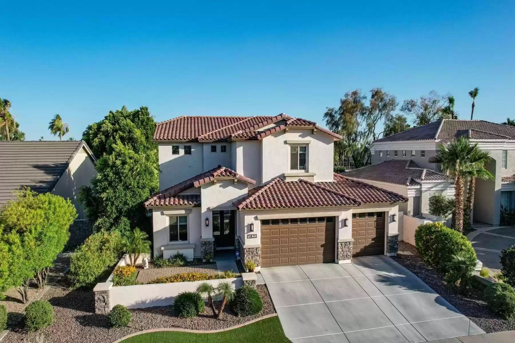 Two-story stucco home with red tile roofs, a three-car garage, and landscaped desert-style yard.