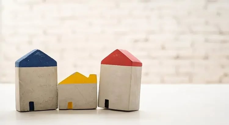 Three small wooden house models painted in blue, red, and yellow, placed on a white surface.